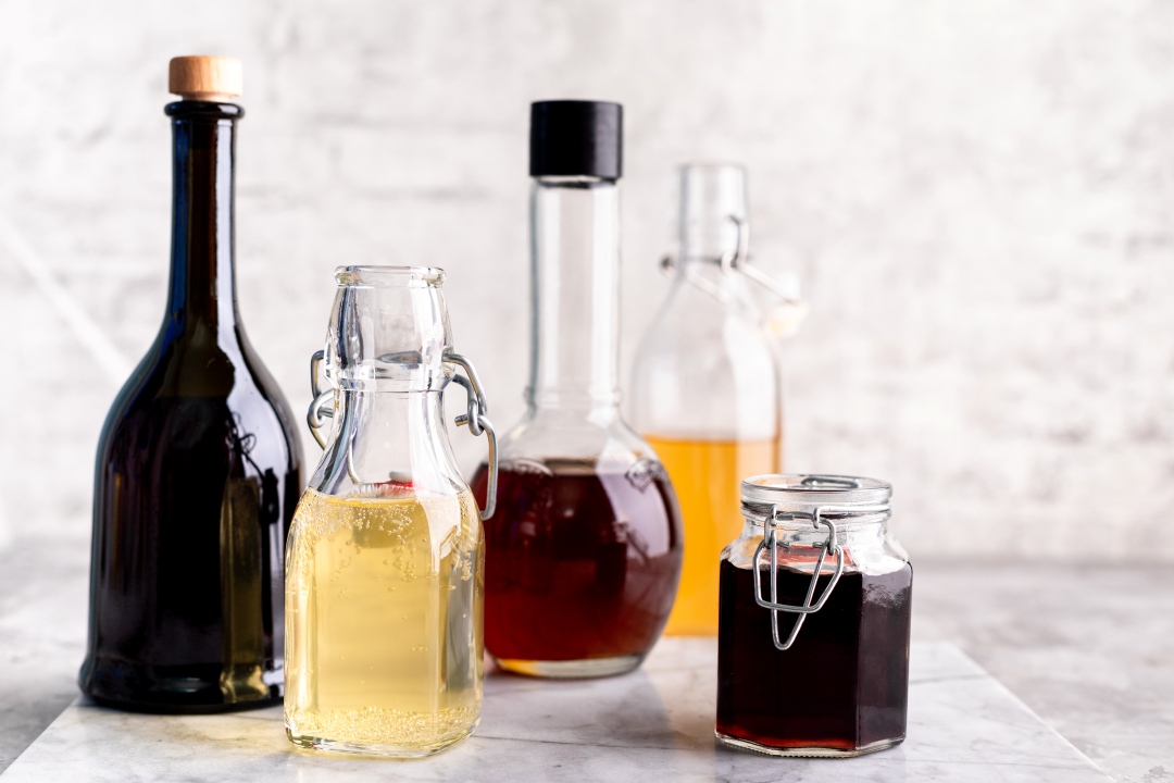 Assorted glass bottles and a jar filled with vinegars and liqueurs on a marble surface