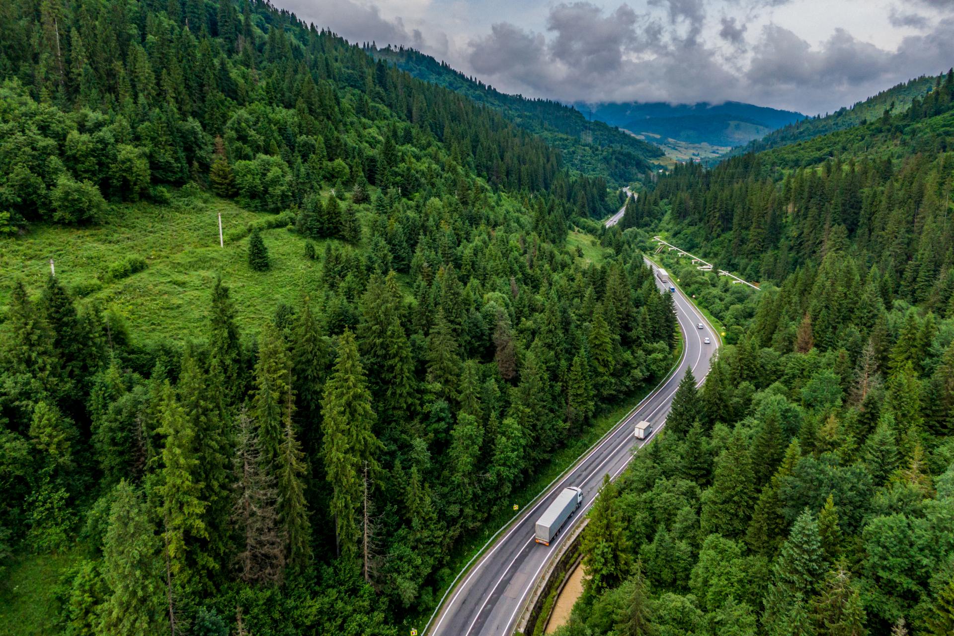 Luftaufnahme einer Straße mit Lkw durch ein bewaldetes Bergtal