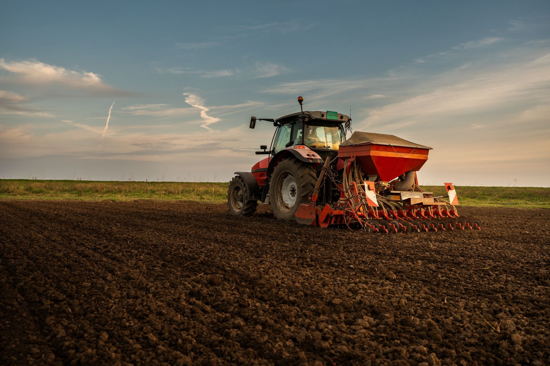 Traktor mit Sämaschine auf einem gepflügten Feld bei Sonnenuntergang [no AI]
