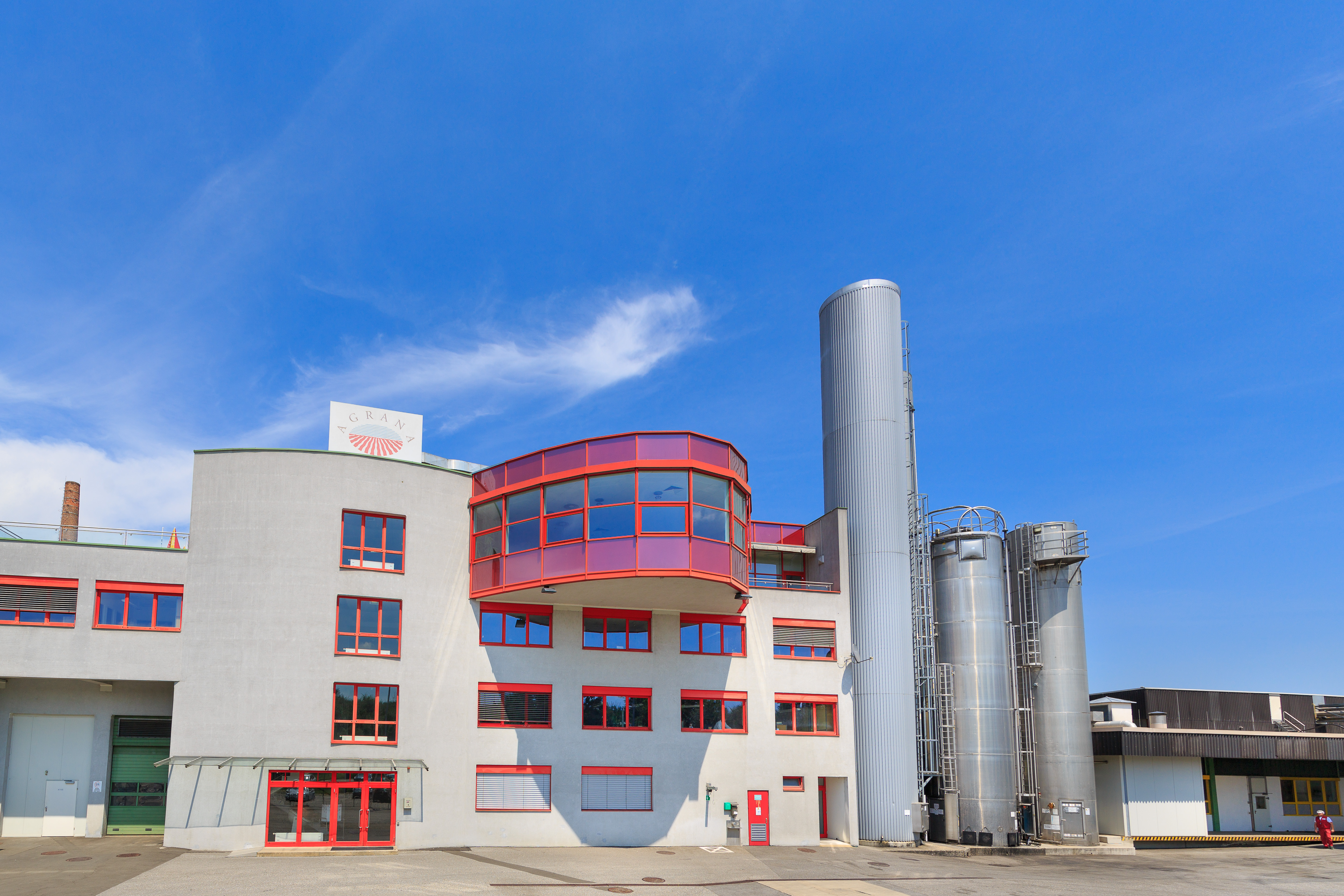 AGRANA Fruit plant in Gleisdorf, Austria: white building with red-framed windows and steel silos under a blue sky [no AI]