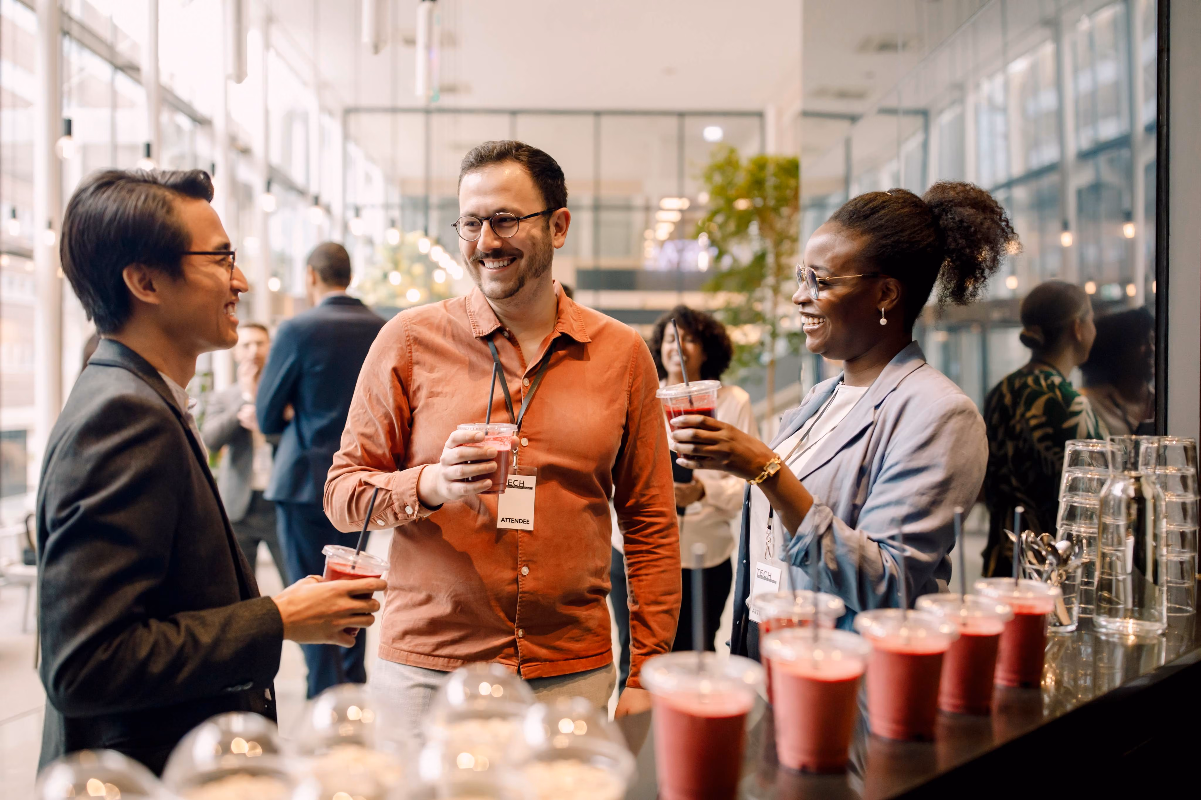 Drei Kolleginnen und Kollegen mit Namensschildern plaudern bei roten Drinks auf einem Networking-Event [no AI]