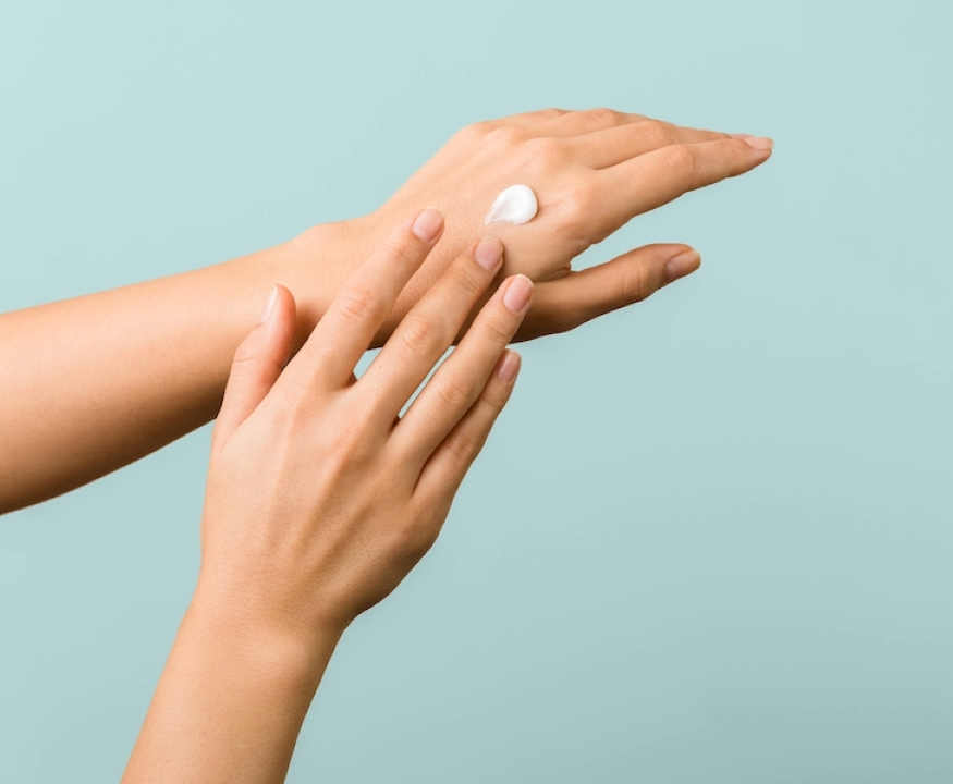 Hände verteilen einen Klecks weiße Creme auf dem Handrücken vor hellblauem Hintergrund
