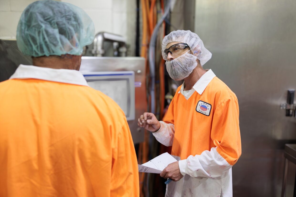 Two production employees in hairnets and orange work jackets discussing a document