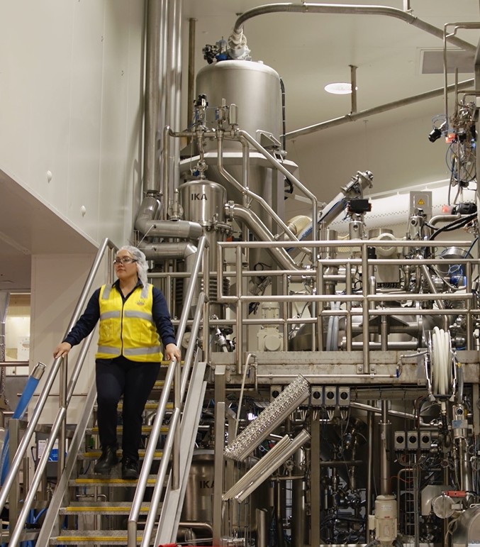 Employee in a high-visibility vest walking down stairs in front of stainless-steel process tanks
