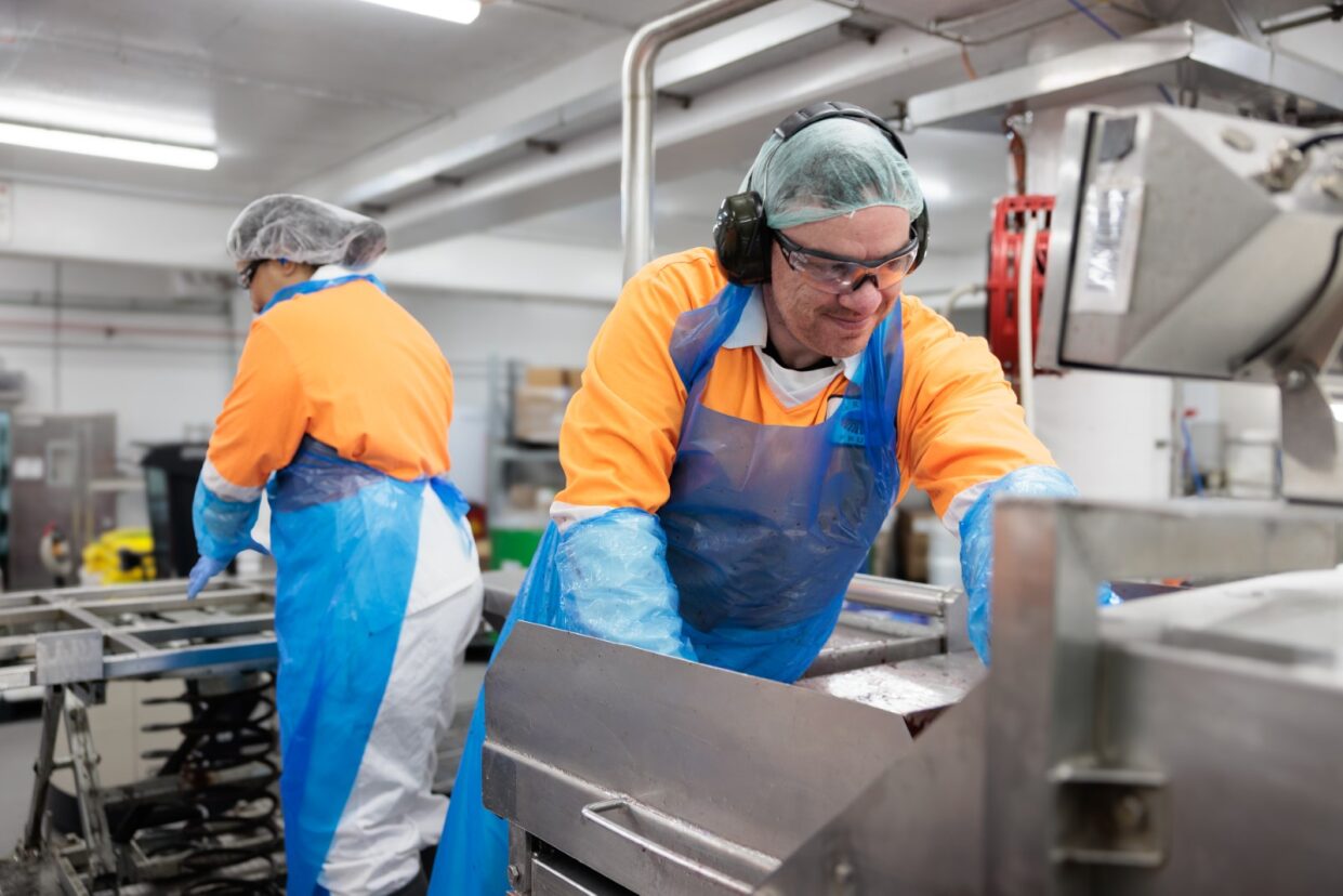 Production employees in orange work jackets, hairnets and aprons at a processing line in the Australian plant
