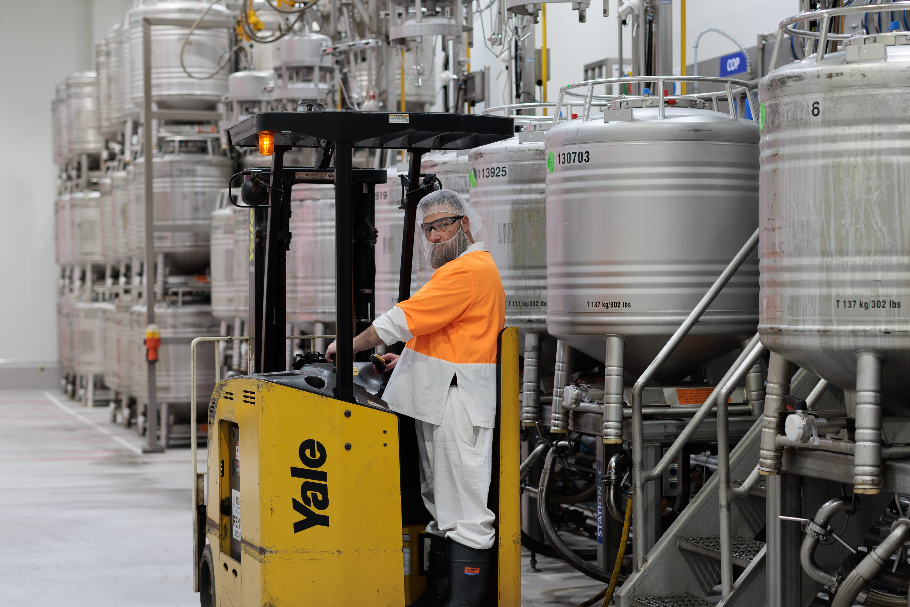 Employee driving a forklift between stainless-steel containers in the Australian plant