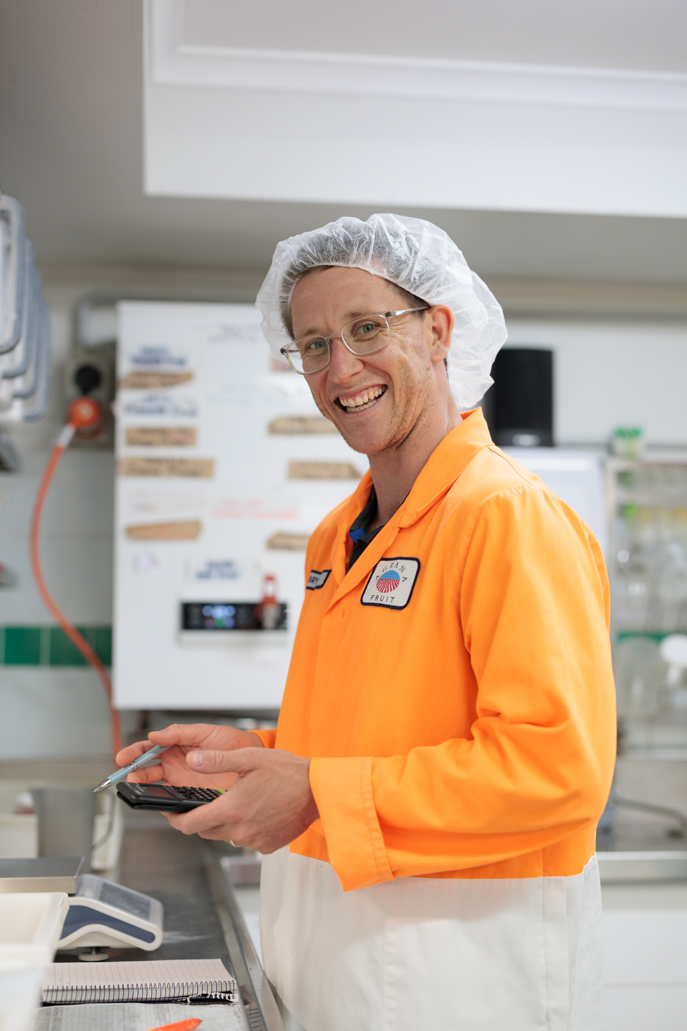Smiling employee in an orange AGRANA Fruit work jacket and hairnet holding a calculator in the plant