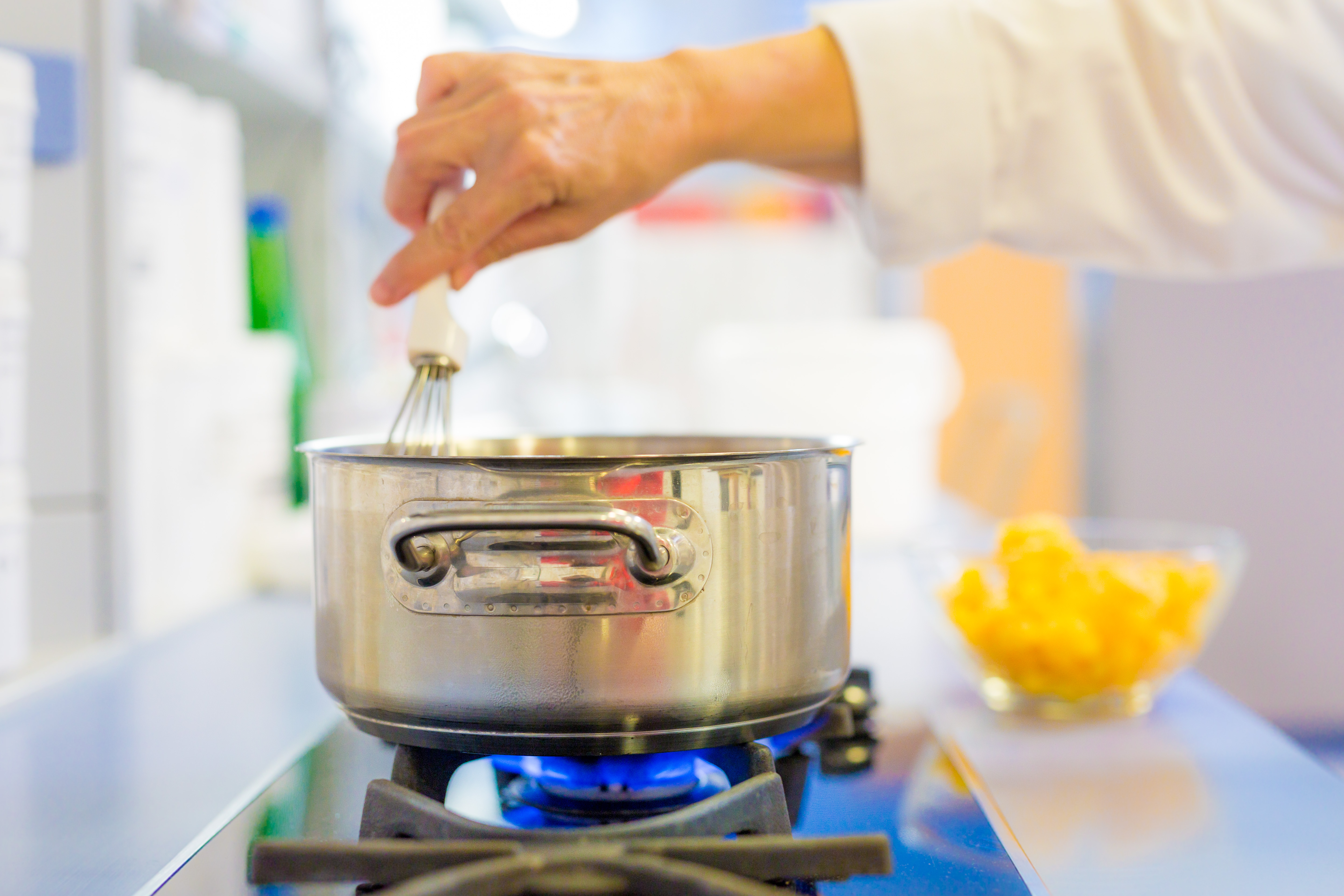 Hand whisking a mixture in a steel pot on a gas burner, a bowl of diced yellow fruit beside it [no AI]