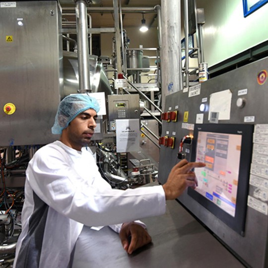 Employee in a white coat and hairnet operating a touchscreen control panel in the Egyptian plant