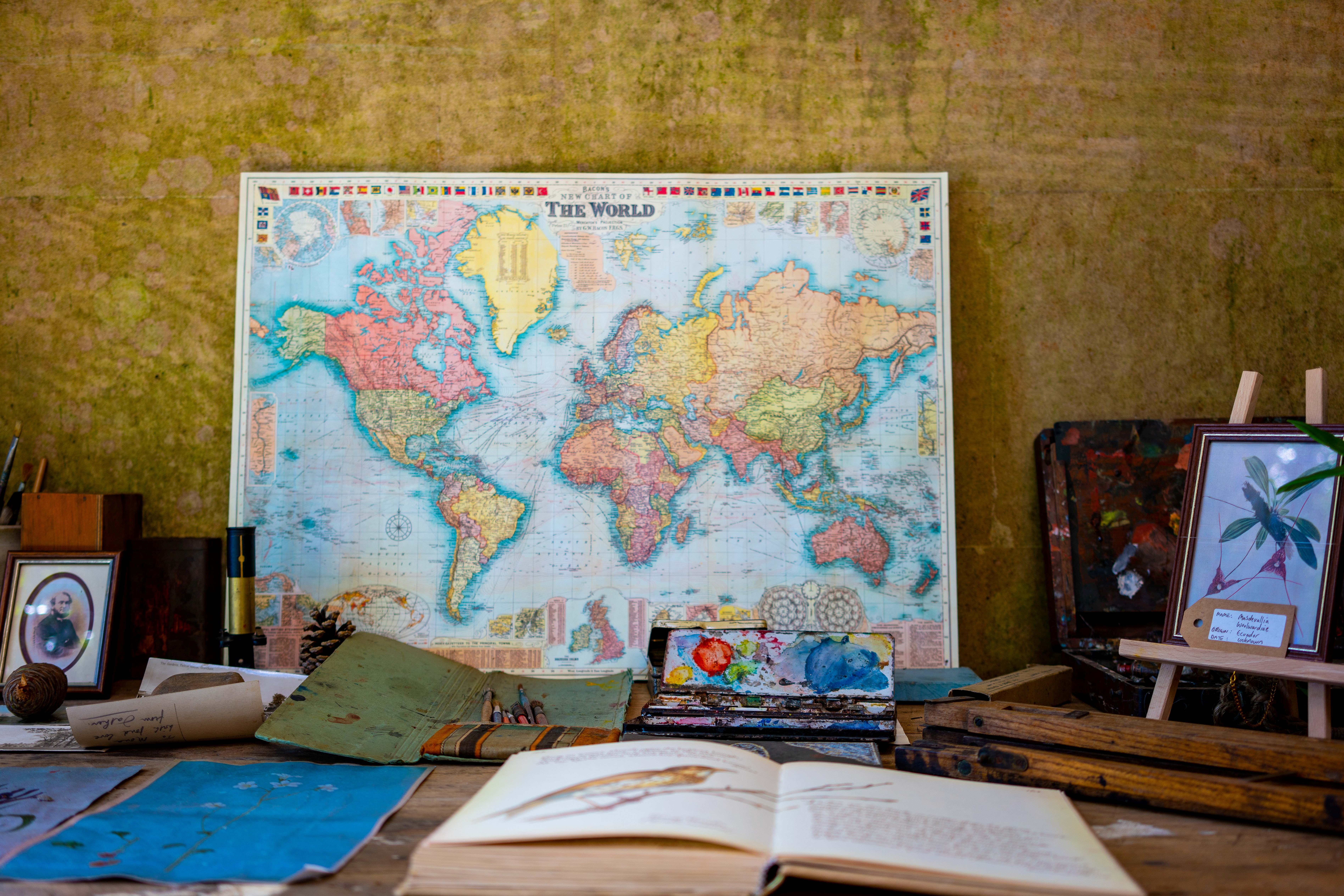 Colourful world map on a wall above a desk with books, drawings and a small easel