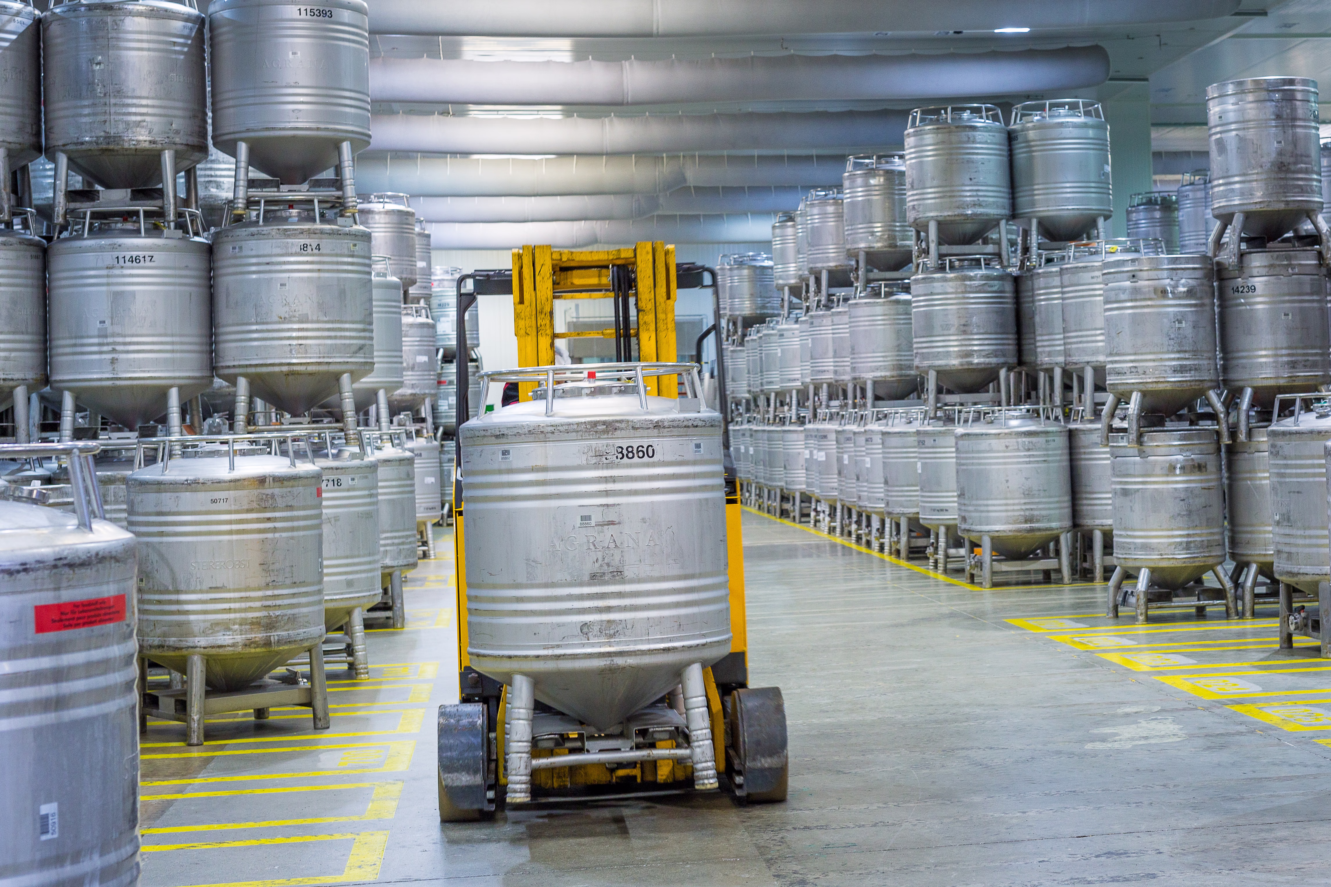Forklift moving a stainless steel AGRANA container through a warehouse full of stacked steel bins