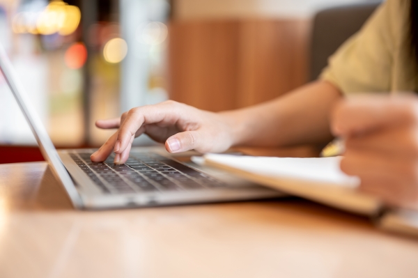 Hand tippt auf einer Laptop-Tastatur, daneben ein Notizbuch