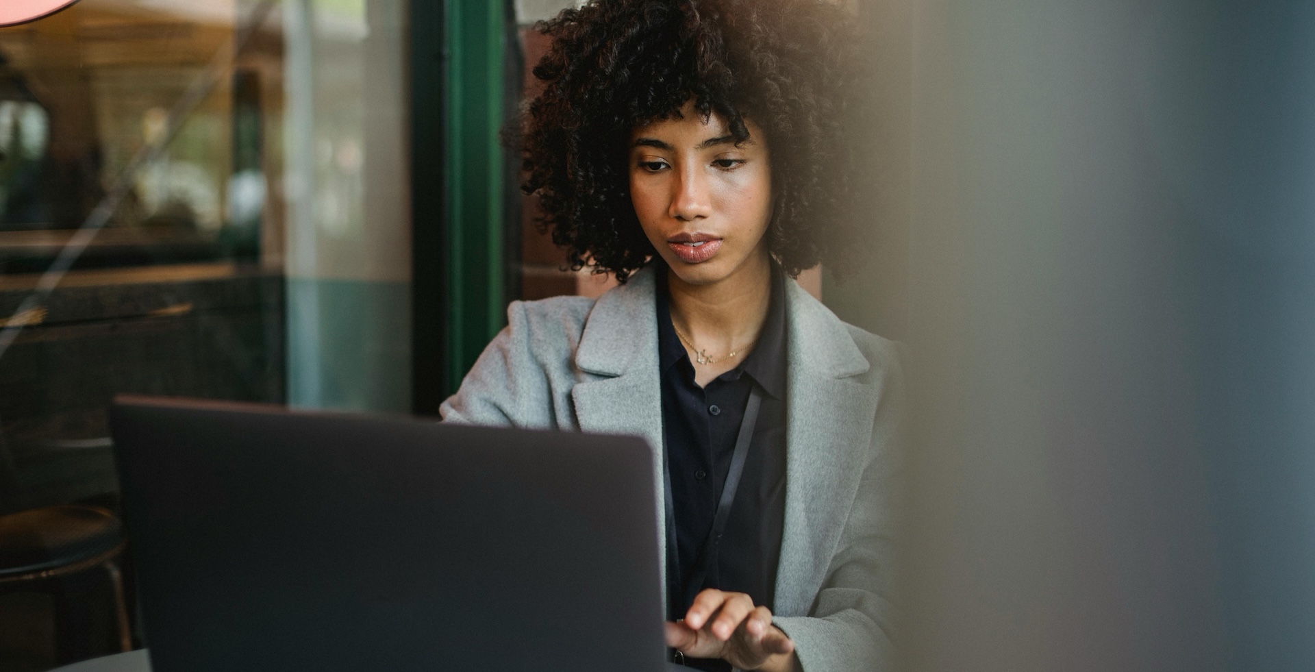 Frau im grauen Blazer arbeitet an einem Laptop an einem Cafétisch