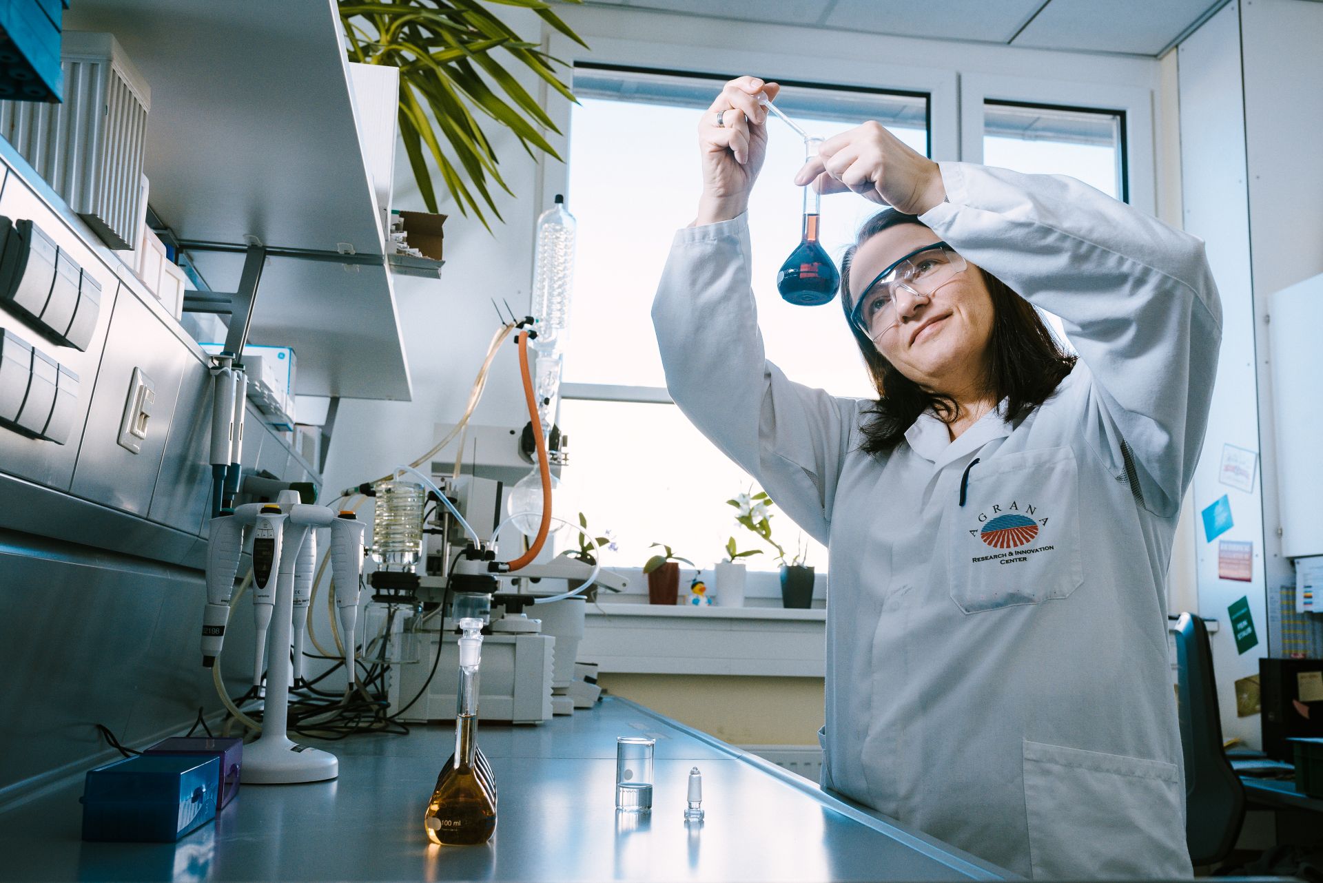 Laborantin mit Schutzbrille prüft einen Kolben im Analytiklabor des ARIC