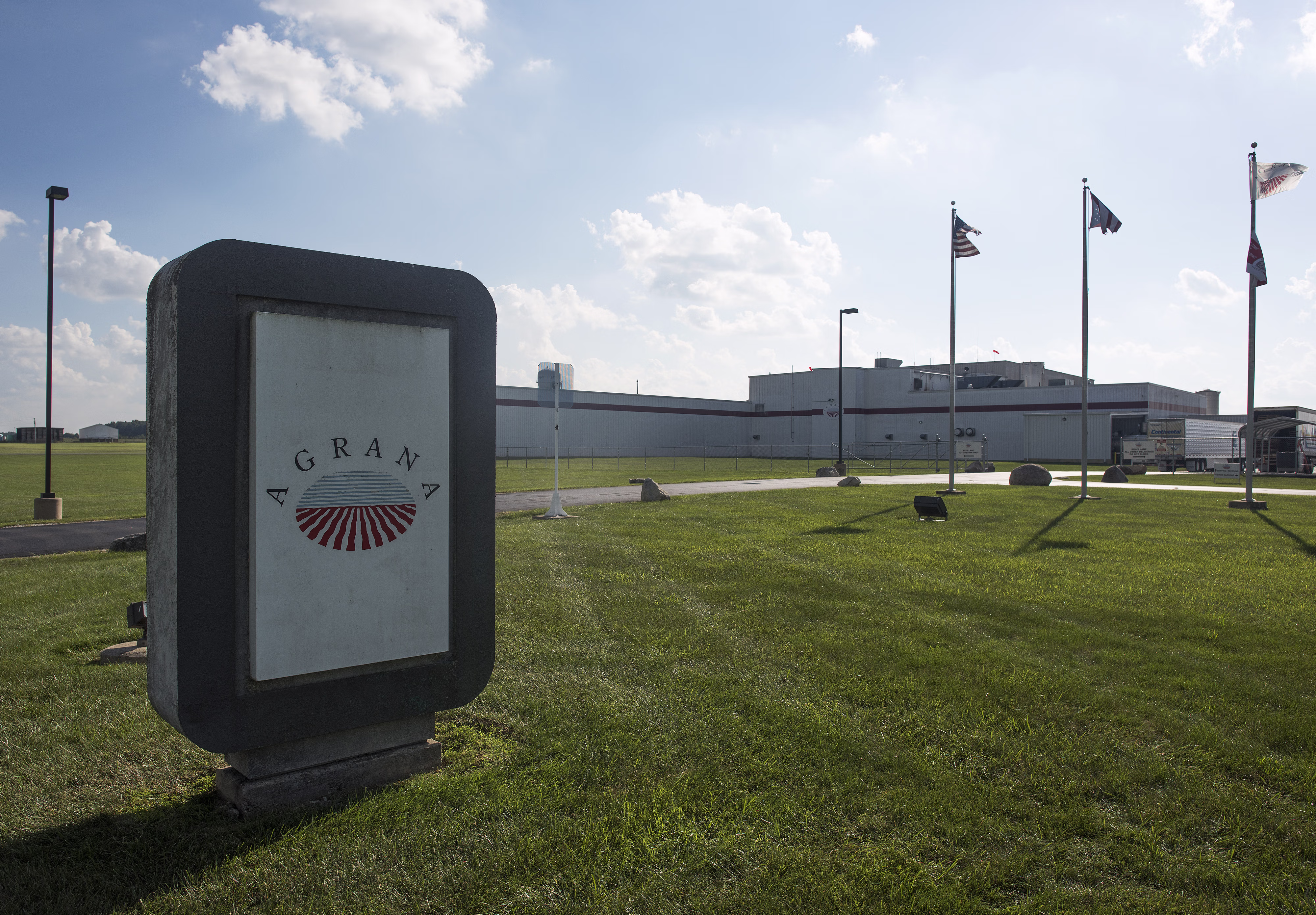 AGRANA sign on a lawn in front of the AGRANA Fruit plant in the USA with flags and plant building [no AI]
