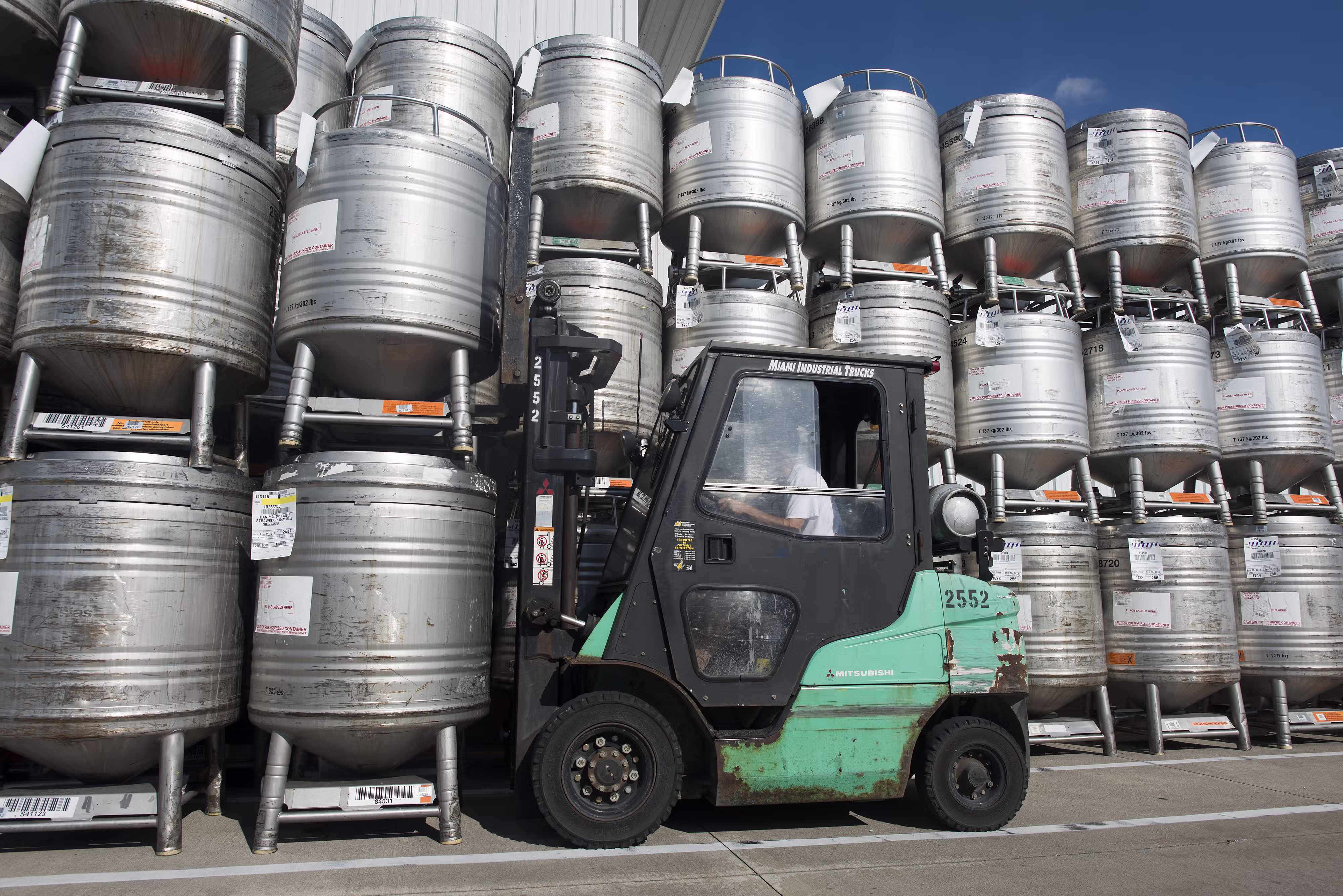 Forklift moving stainless steel containers stacked in front of a US plant [no AI]