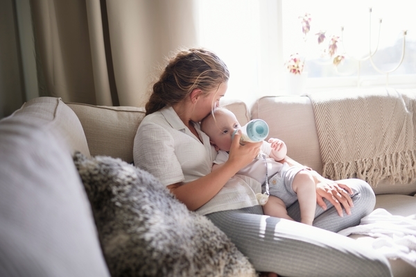 Mutter auf einem Sofa füttert ihr Baby mit dem Fläschchen [no AI]