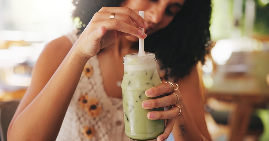 Junge Frau trinkt in einem Café einen Iced Matcha Latte mit Strohhalm