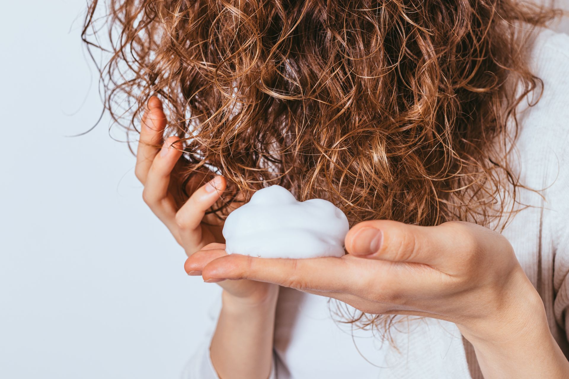 Woman with curly hair holding a dollop of styling foam in her palm