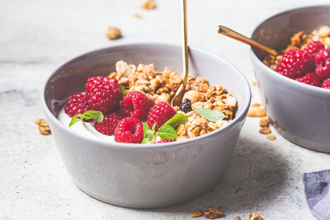 Schale Joghurt mit Granola und frischen Himbeeren, Honig tropft vom Löffel