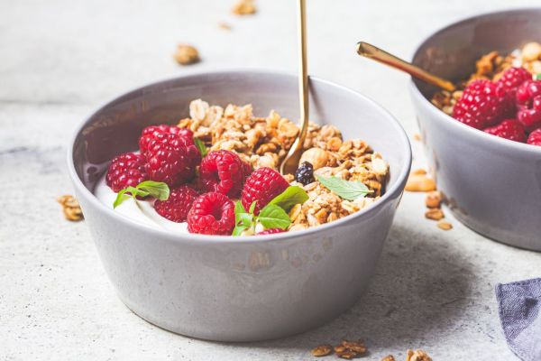 Bowl of yogurt with granola, fresh raspberries and mint, honey being drizzled from a spoon