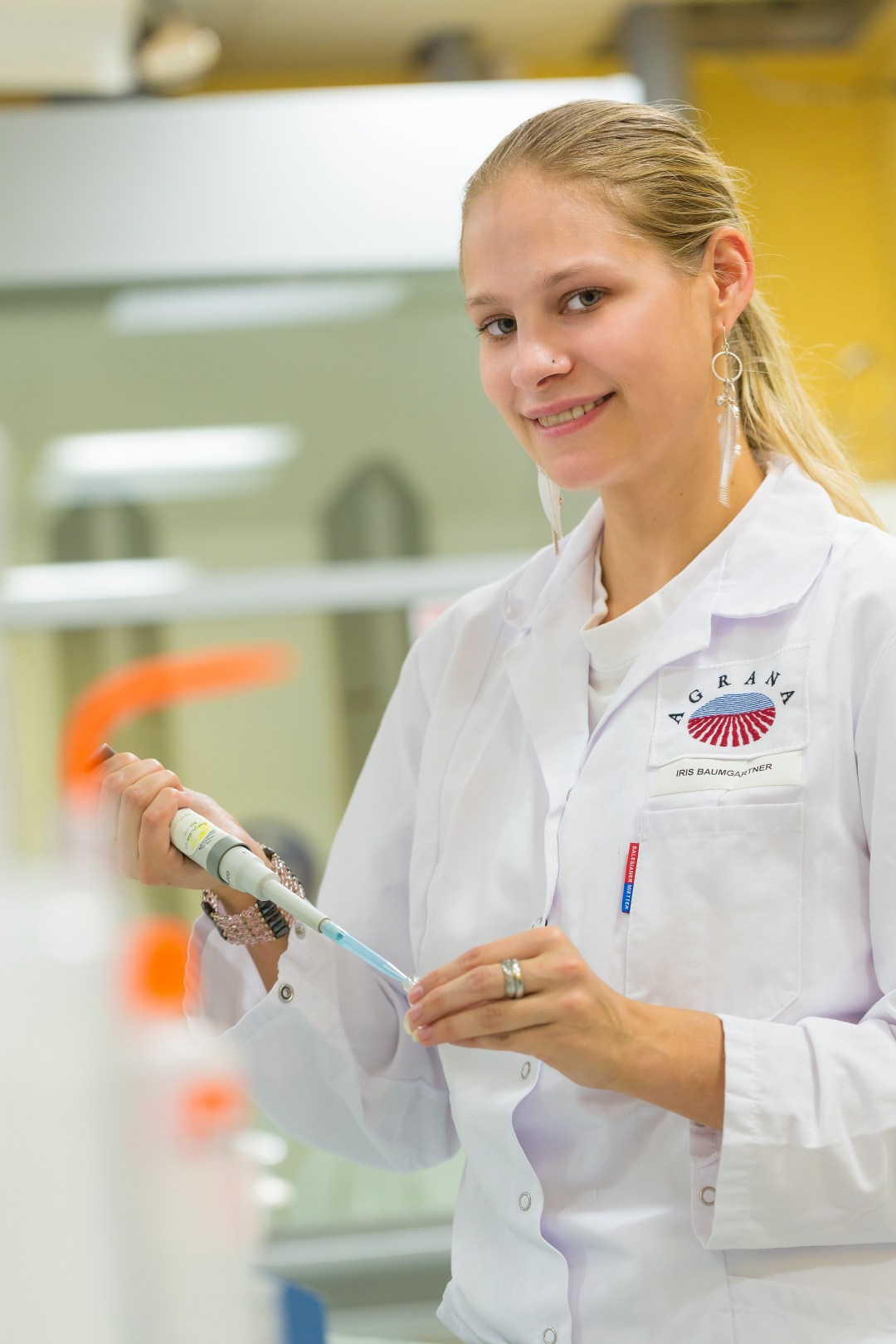 Young lab employee in an AGRANA lab coat holding a pipette