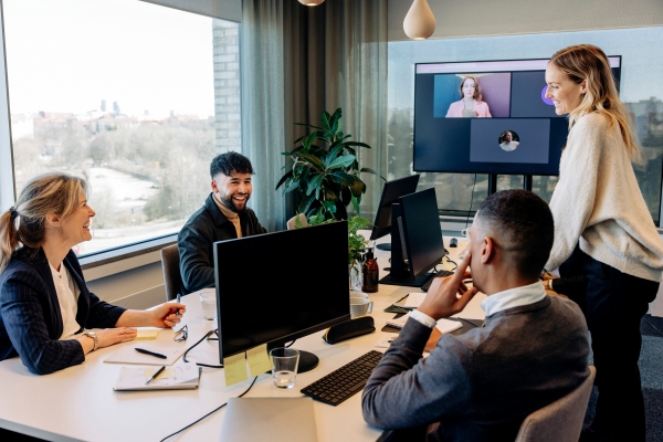 Team in einer Bürobesprechung, Kolleginnen und Kollegen sind per Videocall auf einem großen Bildschirm zugeschaltet [no AI]