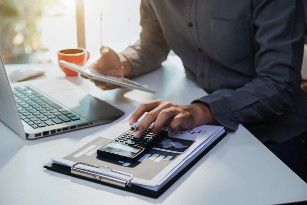 Person arbeitet mit Taschenrechner, Laptop und Finanzdiagrammen am Schreibtisch