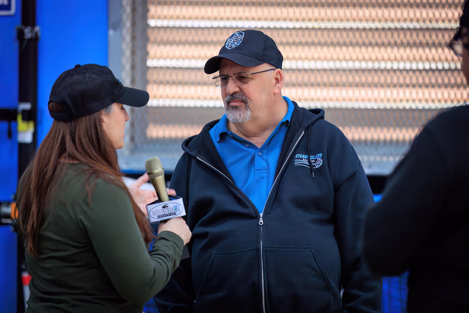 A woman interviewing a man in a blue shirt and black jacket with a microphone labeled Industrial TV.
