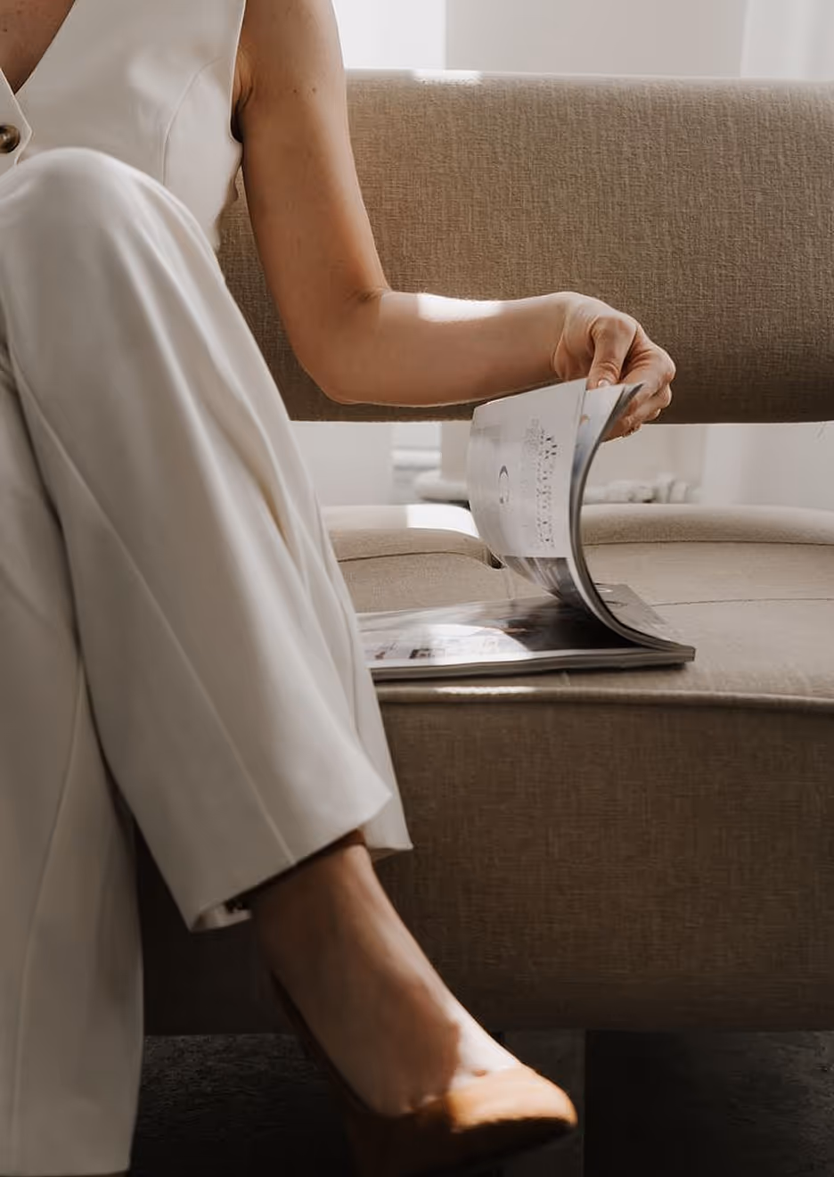 Lady sitting on sofa with magazine reading with one hand in warm room, seeing her only to neck and half for deliberate humor signature.