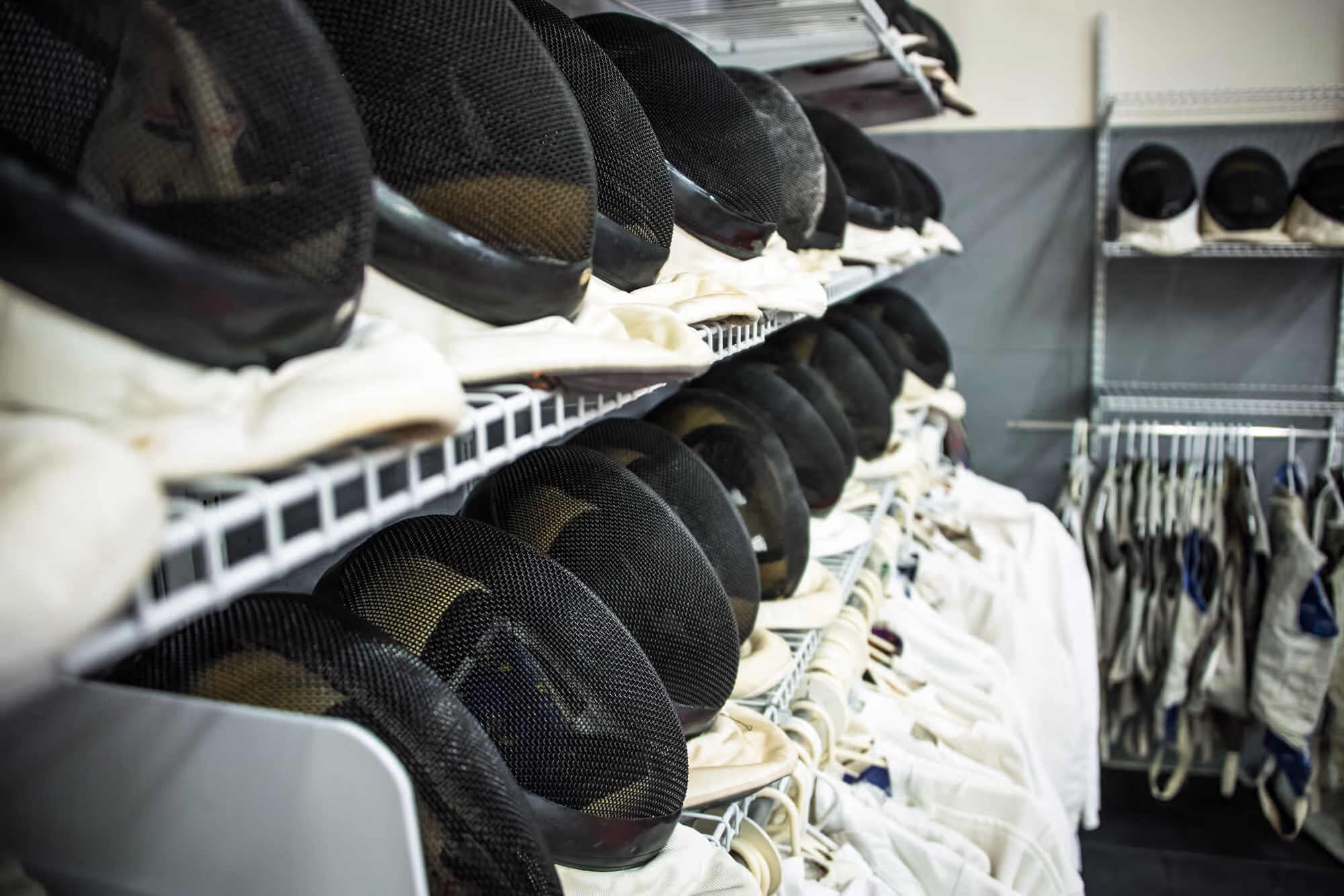 Shelves lined with black fencing masks and white fencing jackets hanging below.