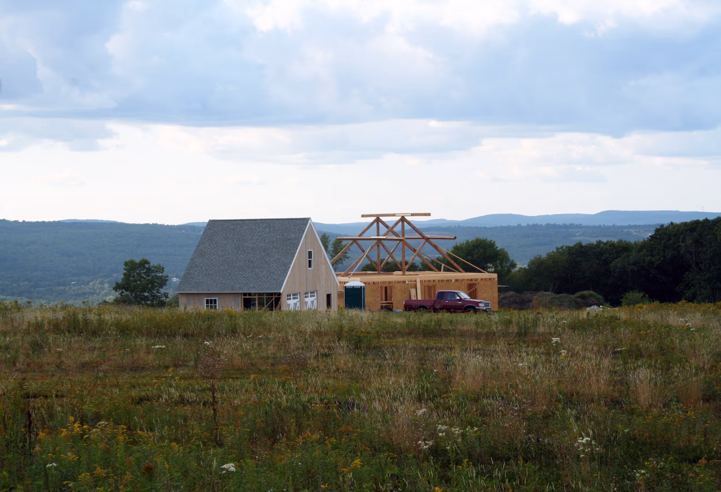 Wooden house under construction in rural field with mountains in background