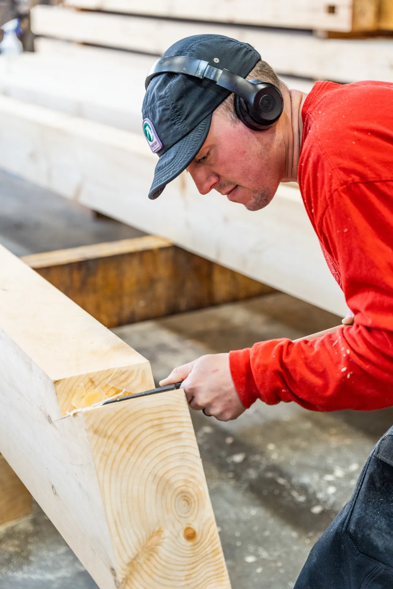 Worker in red shirt and cap measures wooden beam in workshop