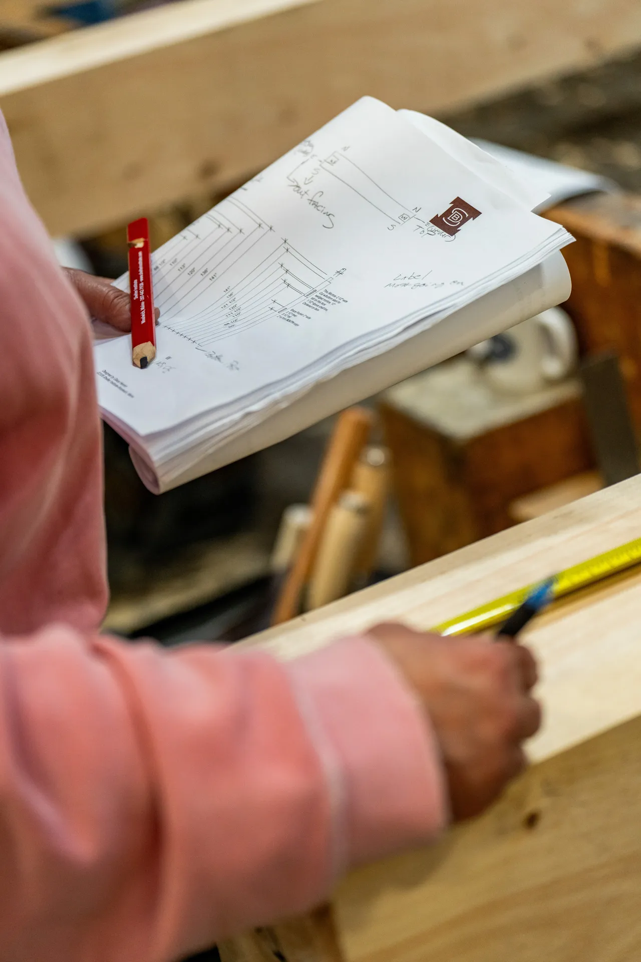 Hands holding technical blueprint and pencil in woodworking workshop