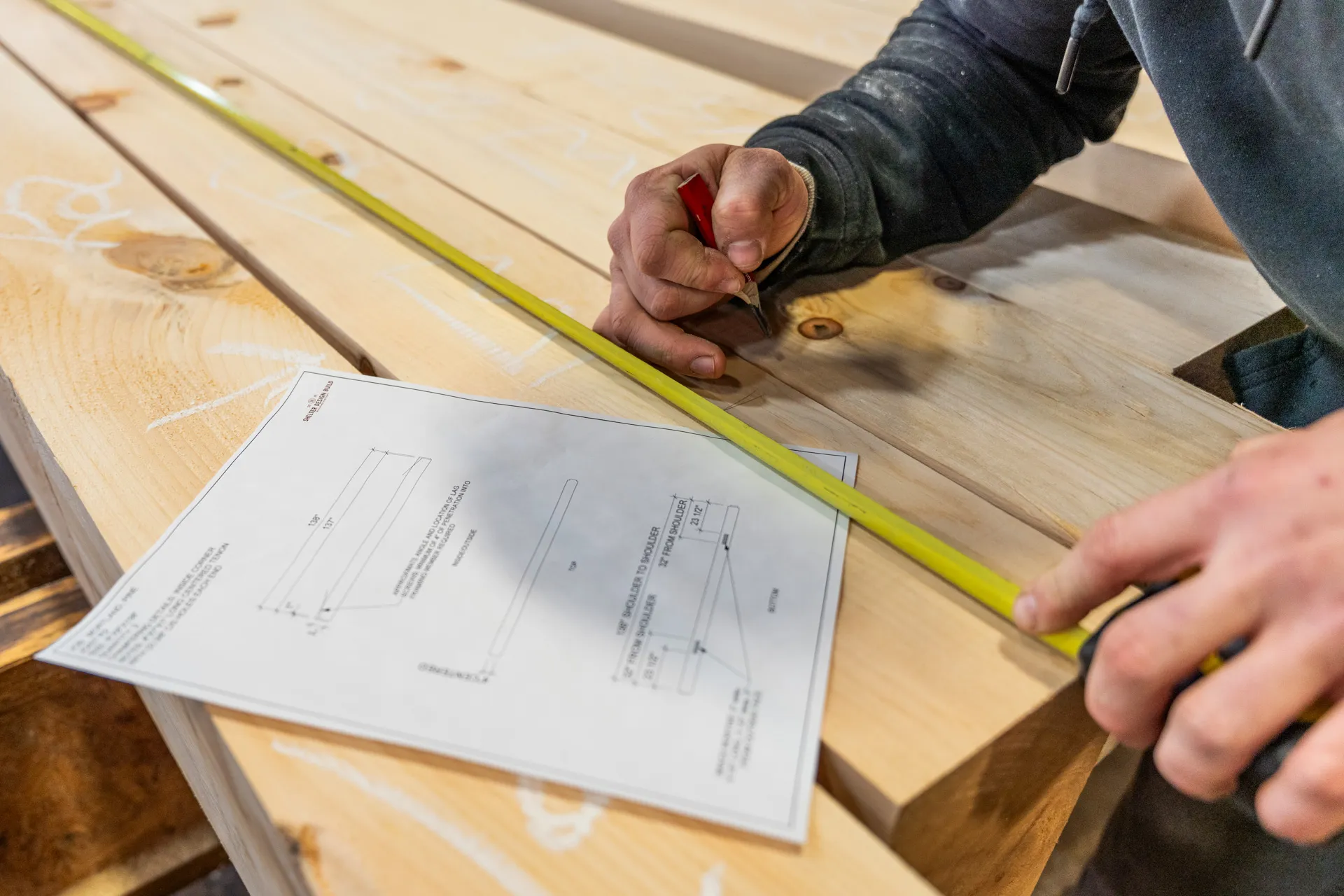 Carpenter measuring wooden board with yellow tape measure and marking document