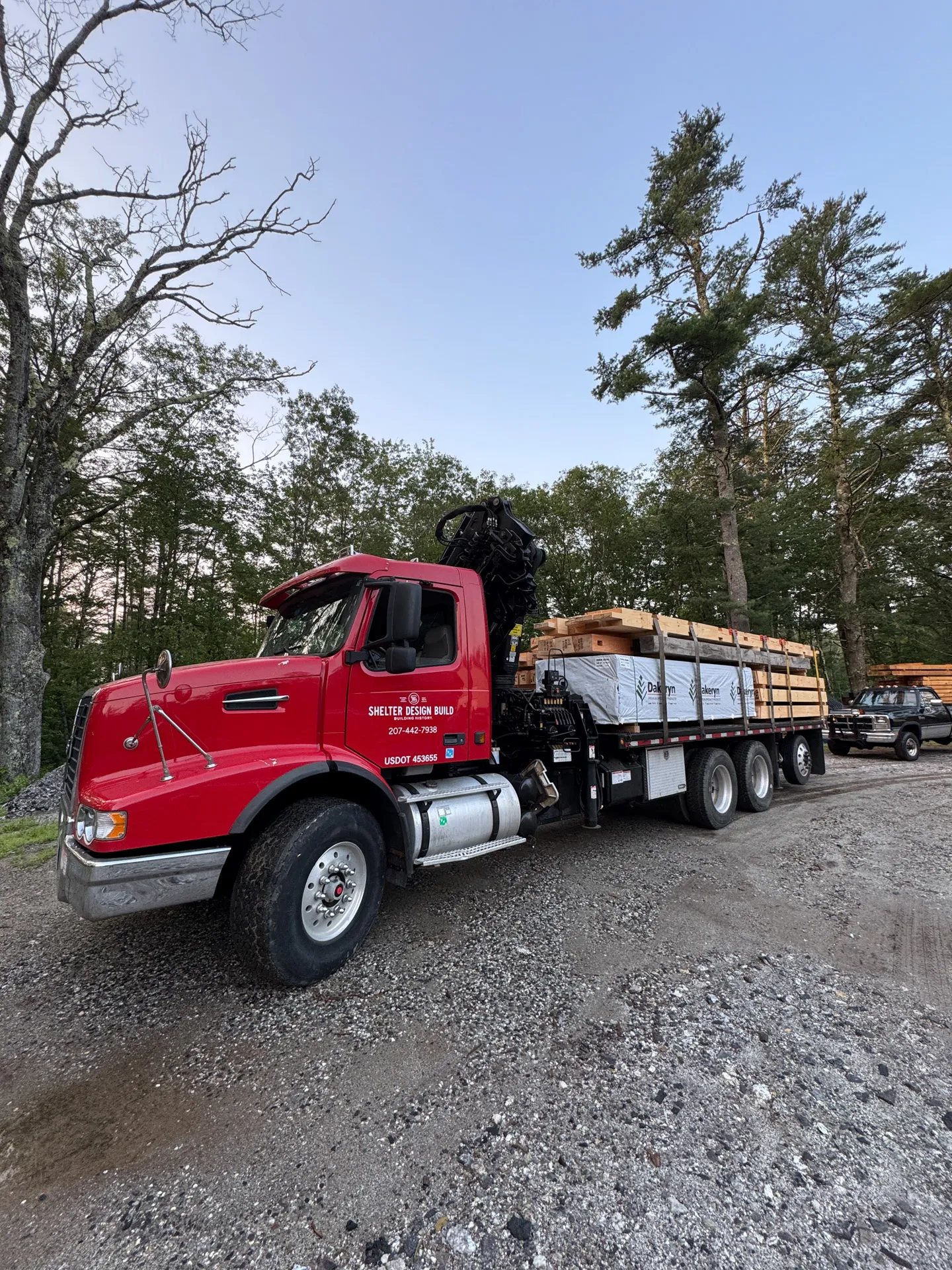 Red truck with construction materials parked in forested gravel area