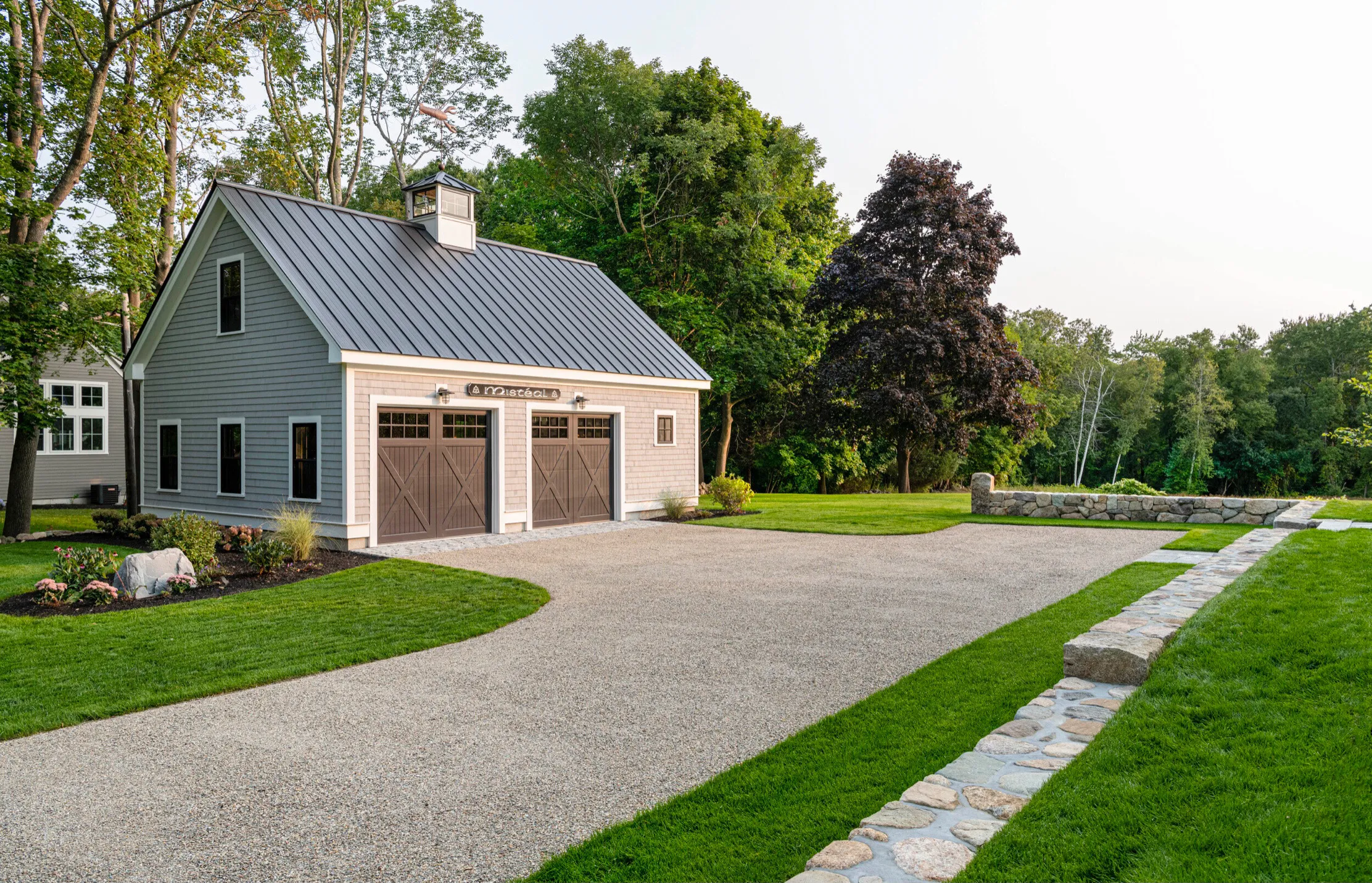 Modern farmhouse garage with metal roof, double doors, surrounded by landscaped lawn and trees