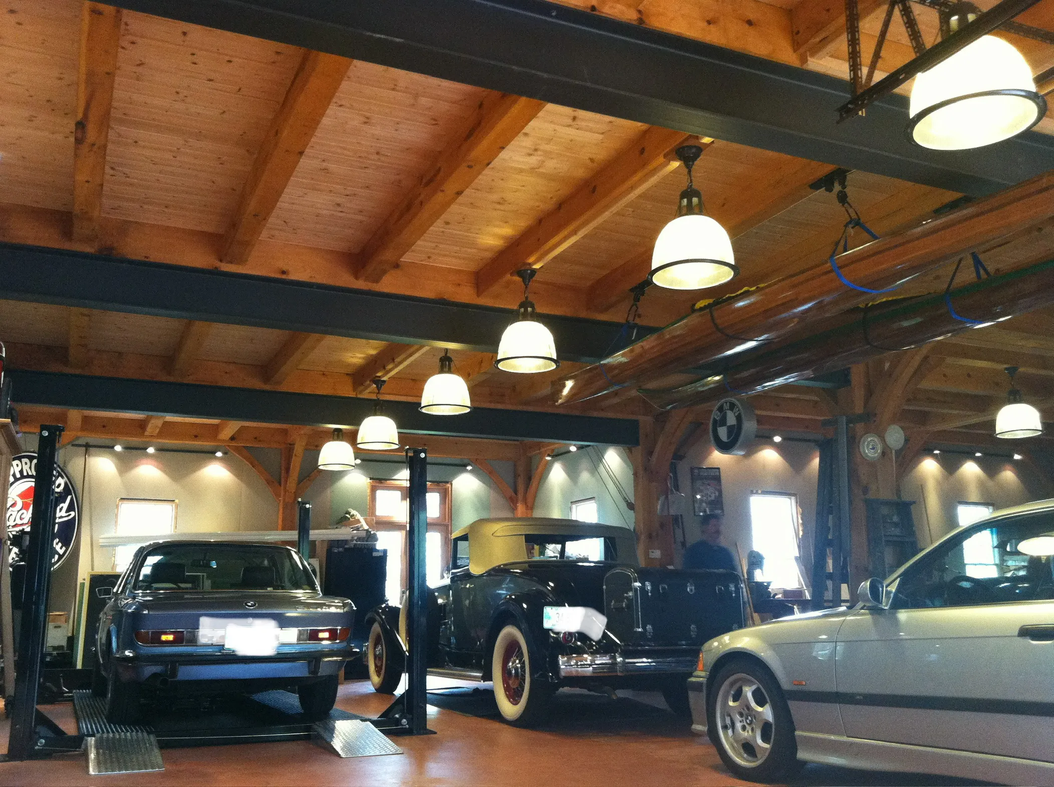 Classic cars displayed in a wooden-beamed garage workshop with pendant lighting.