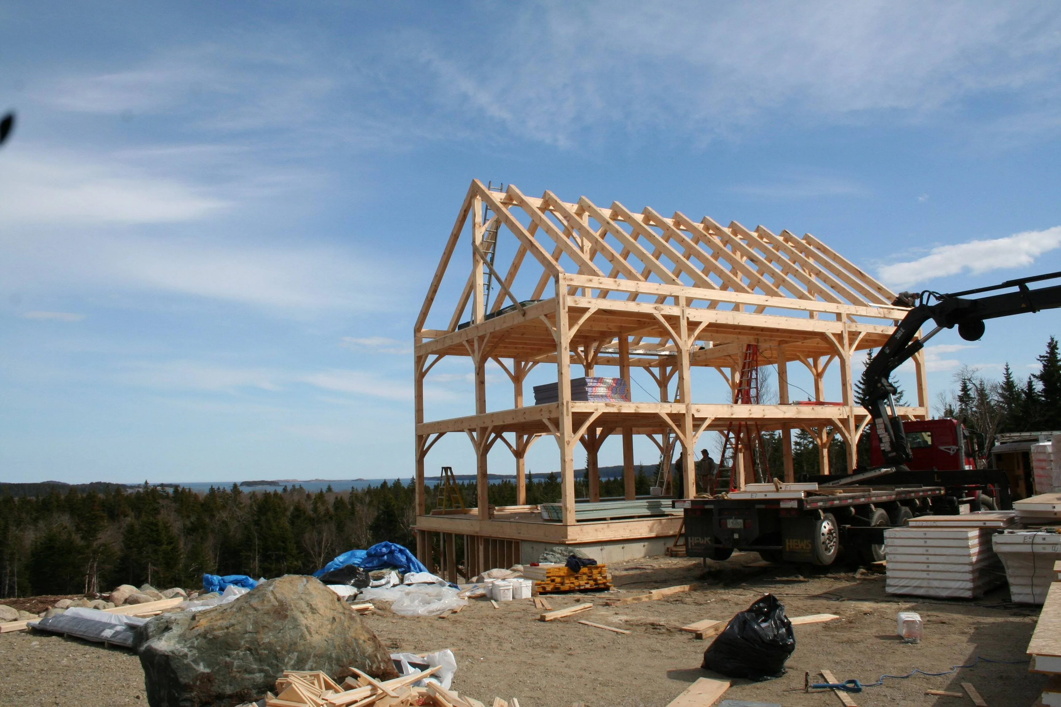 Wooden timber frame house under construction with exposed beams, crane, and construction materials on site