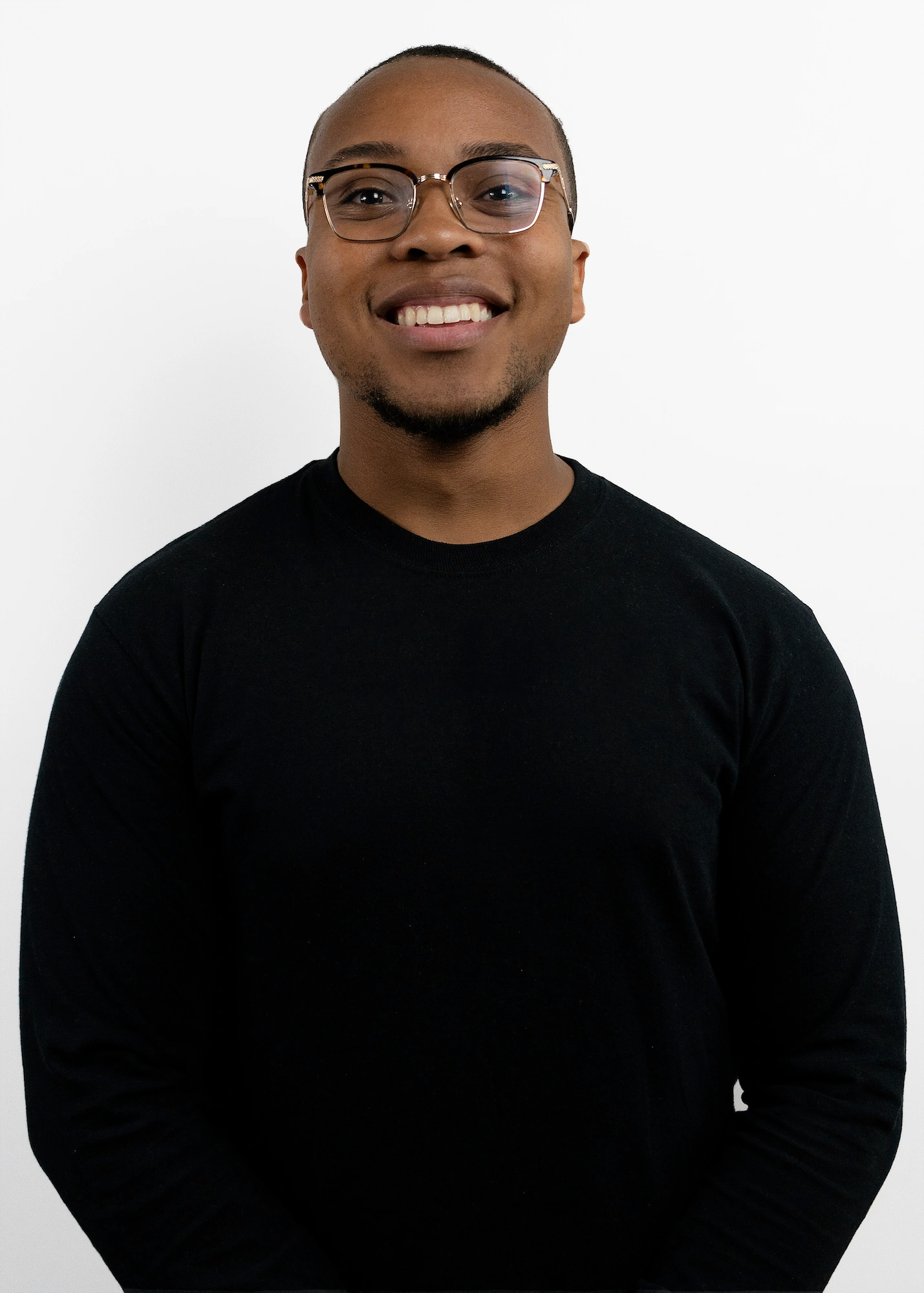 Smiling man wearing glasses and a black long-sleeve shirt against a white background.