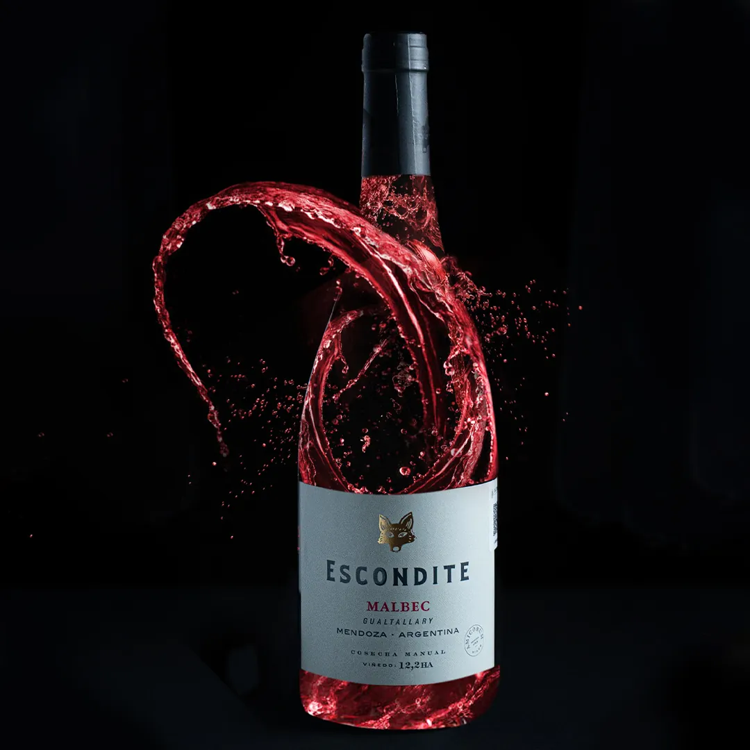Bottle of Escondite Malbec red wine with splash of red wine swirling around against black background.