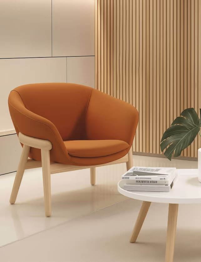 Modern orange armchair with wooden legs next to a white round table holding stacked books and a green leaf in a minimalist room.