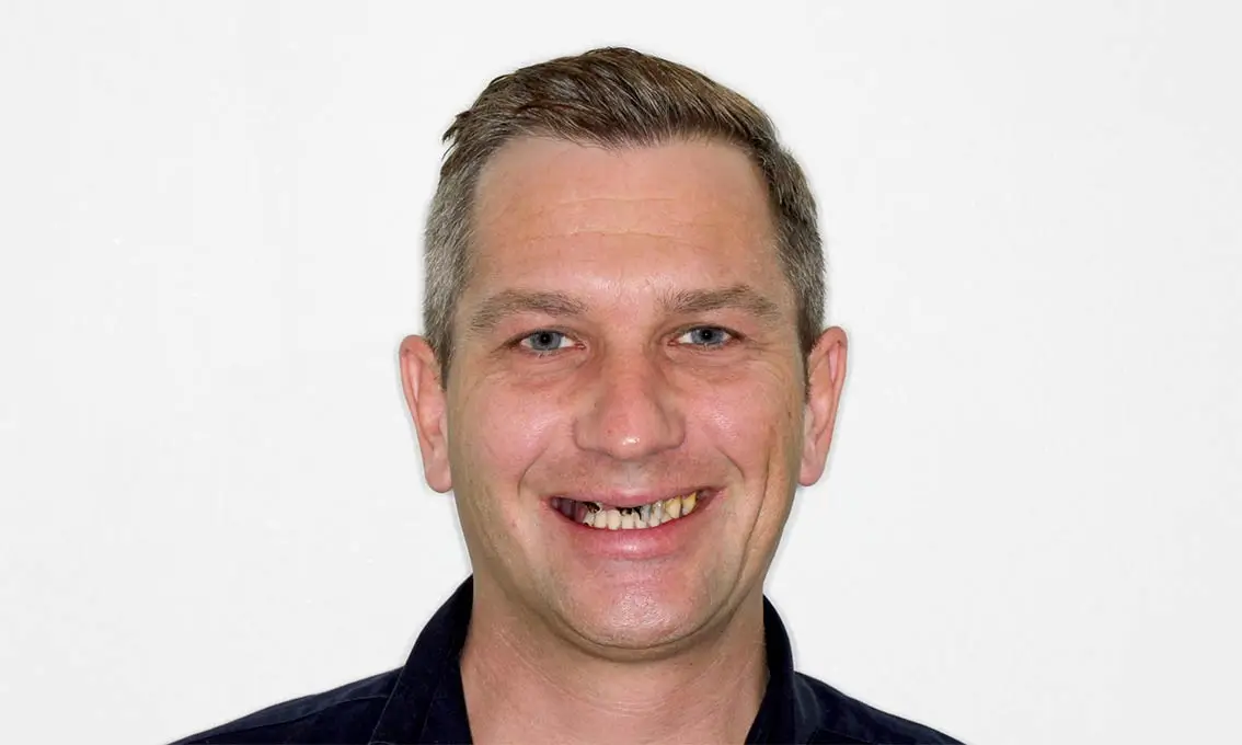 Smiling man with short hair wearing a black shirt against a plain white background.