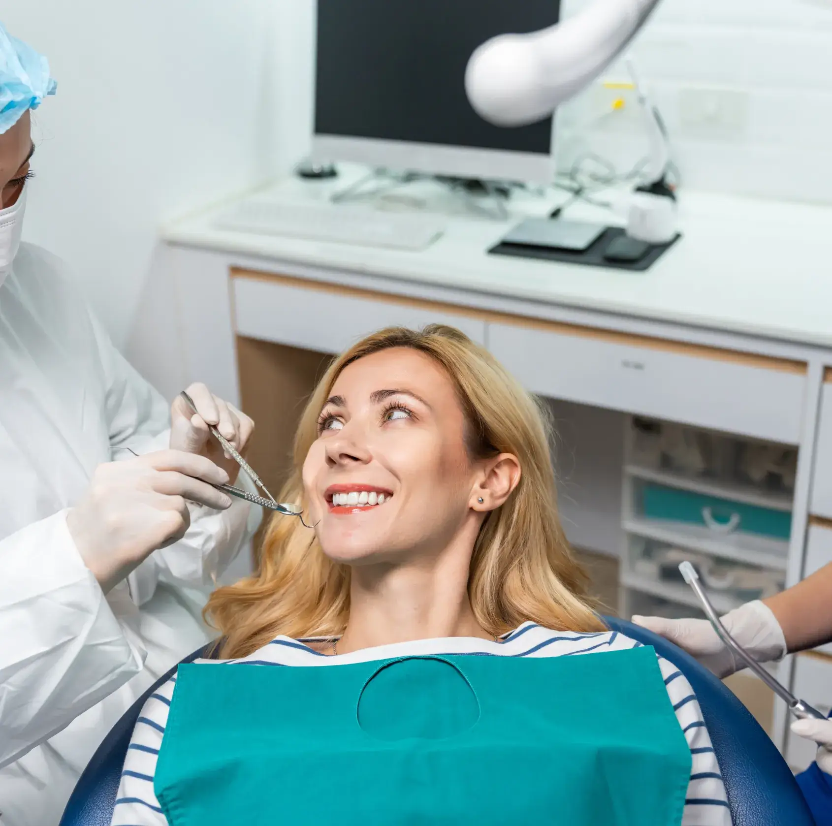 A dentist examines a smiling woman's teeth during a dental check-up.