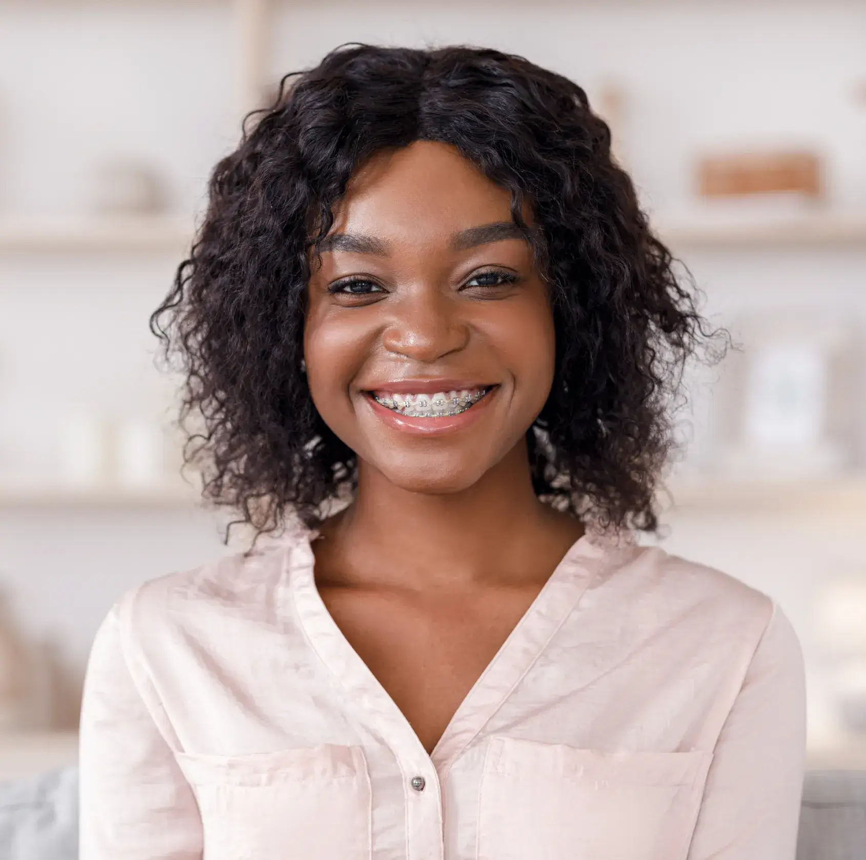 Smiling person with curly hair and braces wearing a pink shirt.