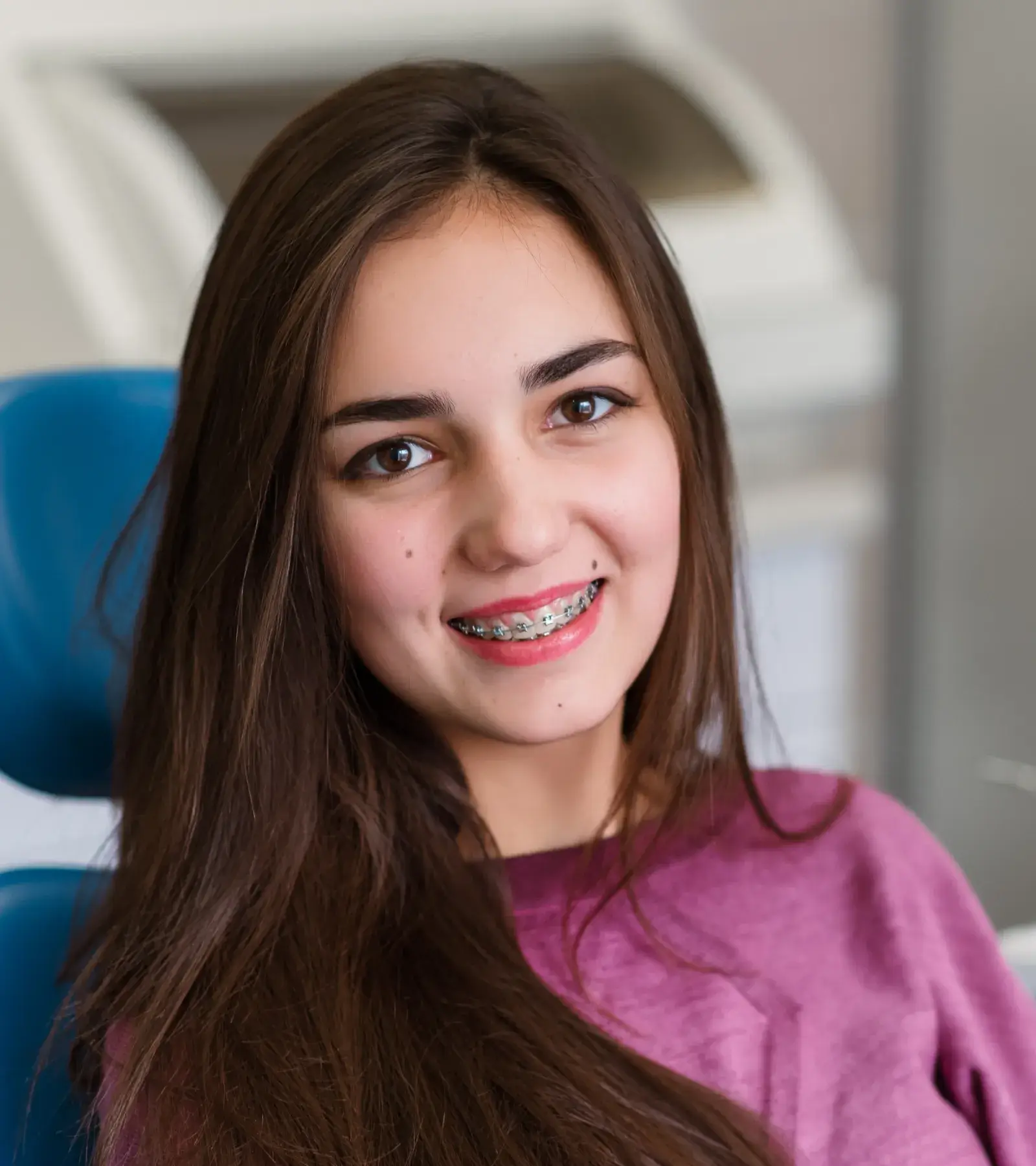 Smiling young woman with braces sitting in a dental chair, wearing a purple top.