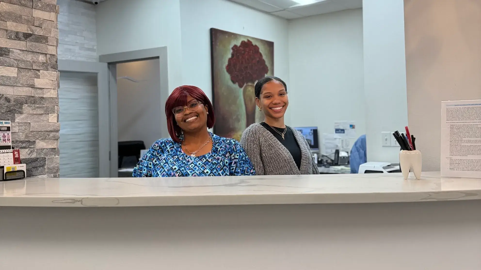 Two women smiling behind a reception desk in an office setting.