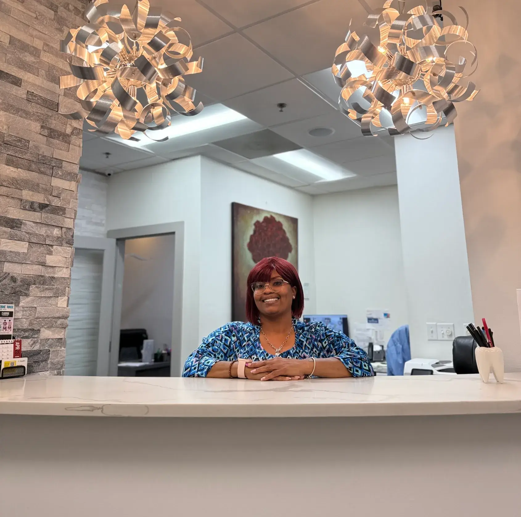A smiling woman stands behind a reception desk, with decorative lights hanging above.