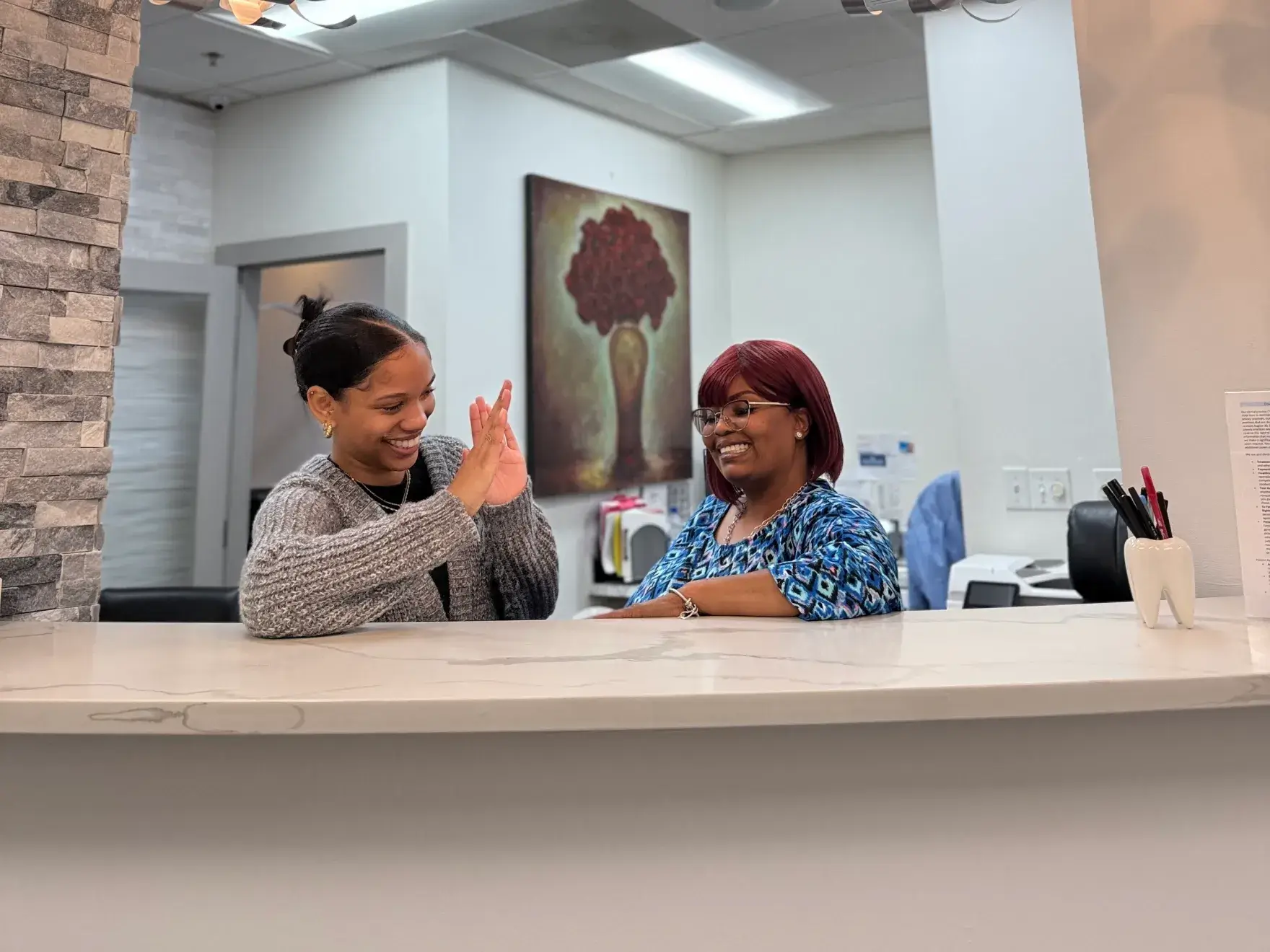 Two women smile and high five each other across a reception desk in an office.