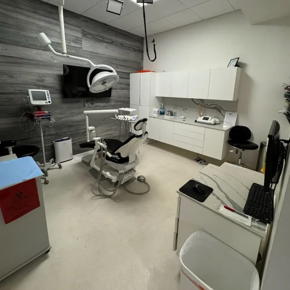 A dental treatment room with a dental chair, overhead light, and various dental equipment.